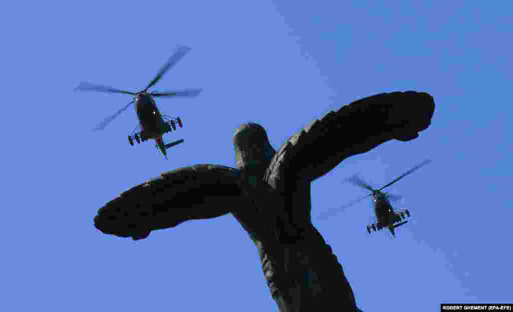 A formation of two military attack helicopters belonging to the Romanian Air Force fly over the Statue of Air Heroes during a ceremony marking Aviation Day and Air Force Day in Bucharest on July 20.
