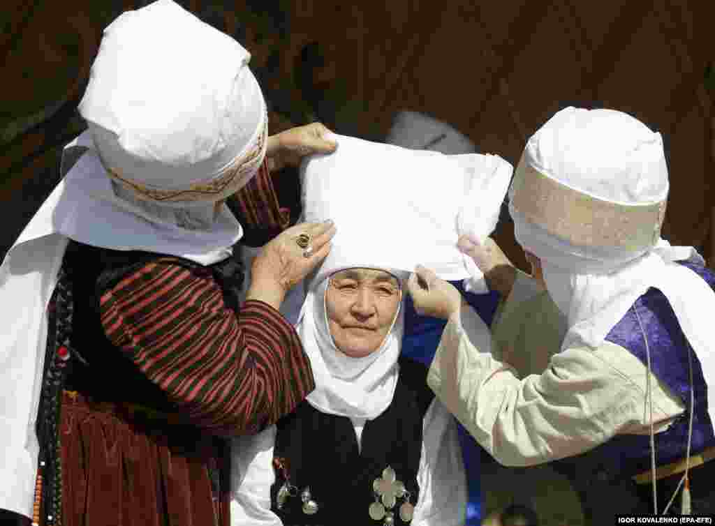 Several woman help another don a traditional hat in Bishkek.