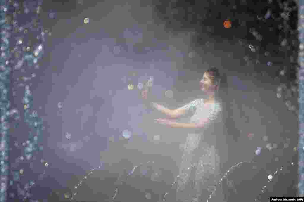 A girl takes a photo as she is engulfed by mist from a public fountain in Bucharest.