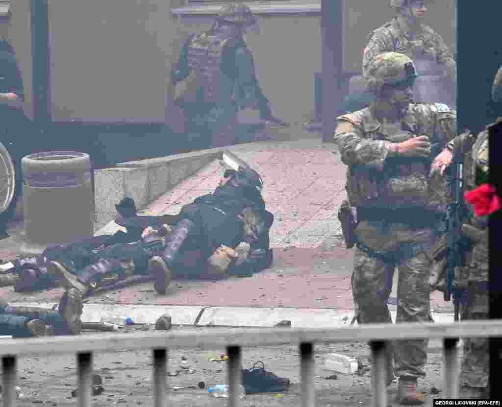 Injured KFOR troops lie on the ground after an attack as U.S. soldiers (right) direct other members of the peacekeeping force.&nbsp;&nbsp;