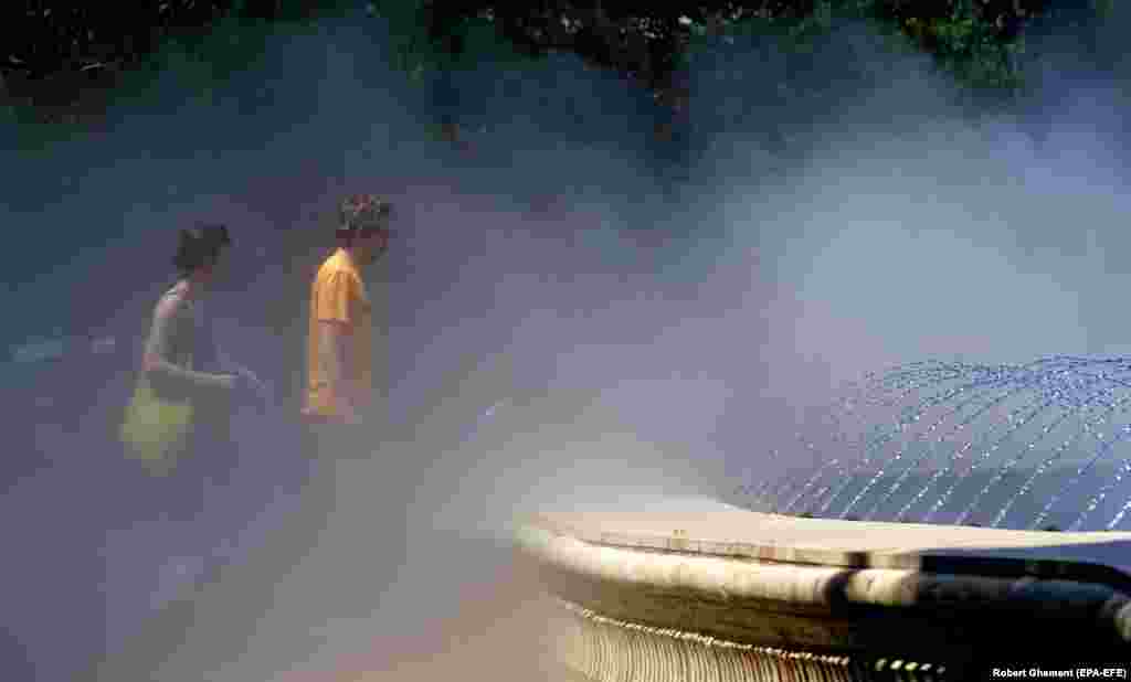 A couple walks through a cooling water mist on a scorching summer&#39;s day in Bucharest.