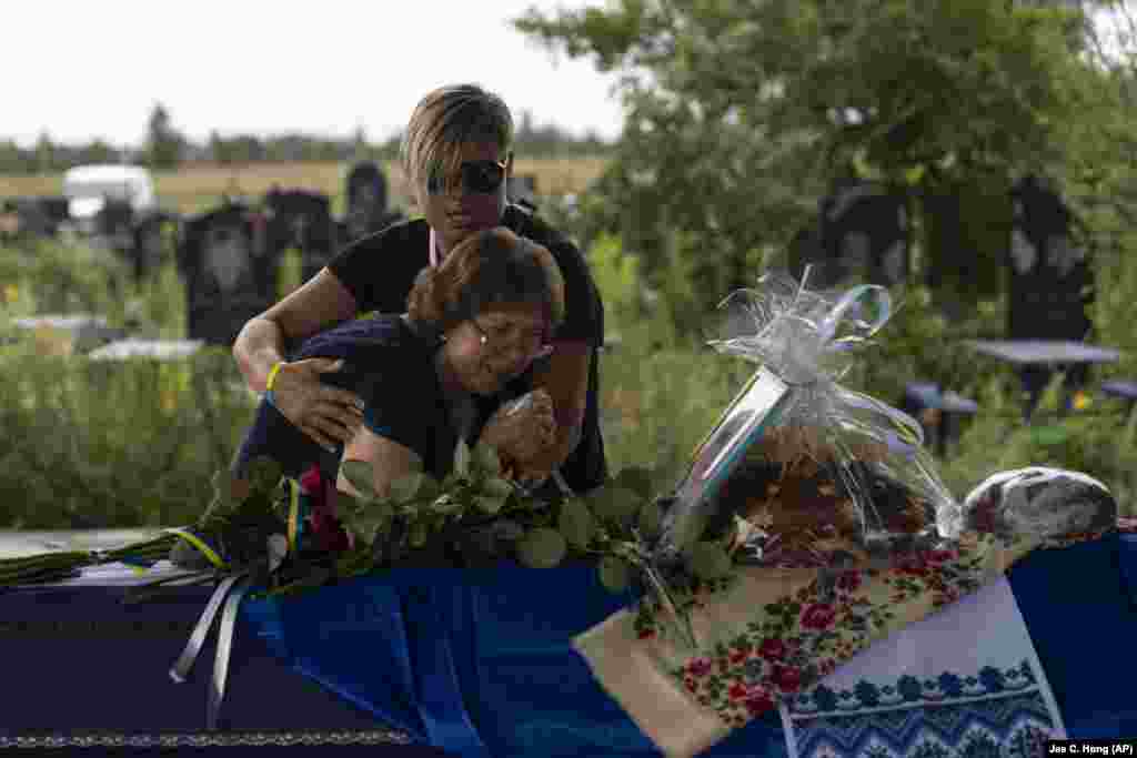 Comforted by Krystyna Liubymska, Zenaida Nedoleshko weeps next to a casket carrying the remains of her nephew, Roman Shadlovskiy, during a reburial service for him in Bucha, Ukraine.