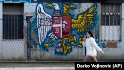 A girl walks by a mural on a wall that shows the Serbian (left) and Russian coats of arms in Belgrade.