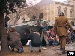 A group of anti-communist civilian fighters along with a Romanian soldier supporting anti-Ceausescu activists protect themselves from sniper fire behind an armored personnel carrier on December 24, 1989.