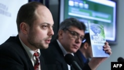 Vladimir Kara-Murza (left) holds up a copy of the report on corruption at the 2014 Sochi Olympics as Russian opposition leader Boris Nemtsov listens during a news conference on January 30, 2014, at the National Press Club in Washington, D.C.